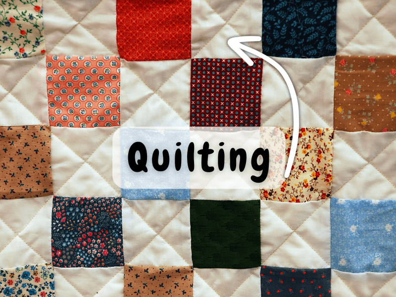 A close-up of a patchwork quilt made of colourful fabric squares stitched in a diagonal grid pattern. The word 'Quilting\' is written on a label overlay, with an arrow pointing to the visible quilting stitches that run across the blocks.