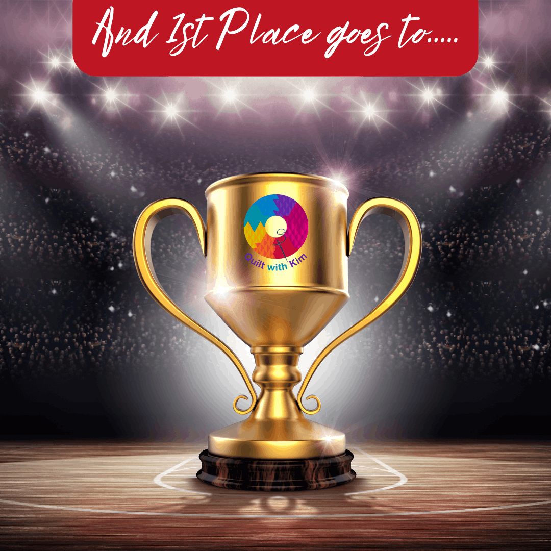 A gold trophy with a colorful Quilt with Kim logo stands on a wooden base under bright stadium lights. Above, a red banner reads, And 1st Place goes to....