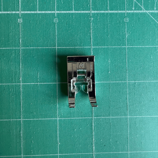 Open-toe sewing machine foot shown on a green cutting mat, used to give a clear view of the stitching line while sewing.